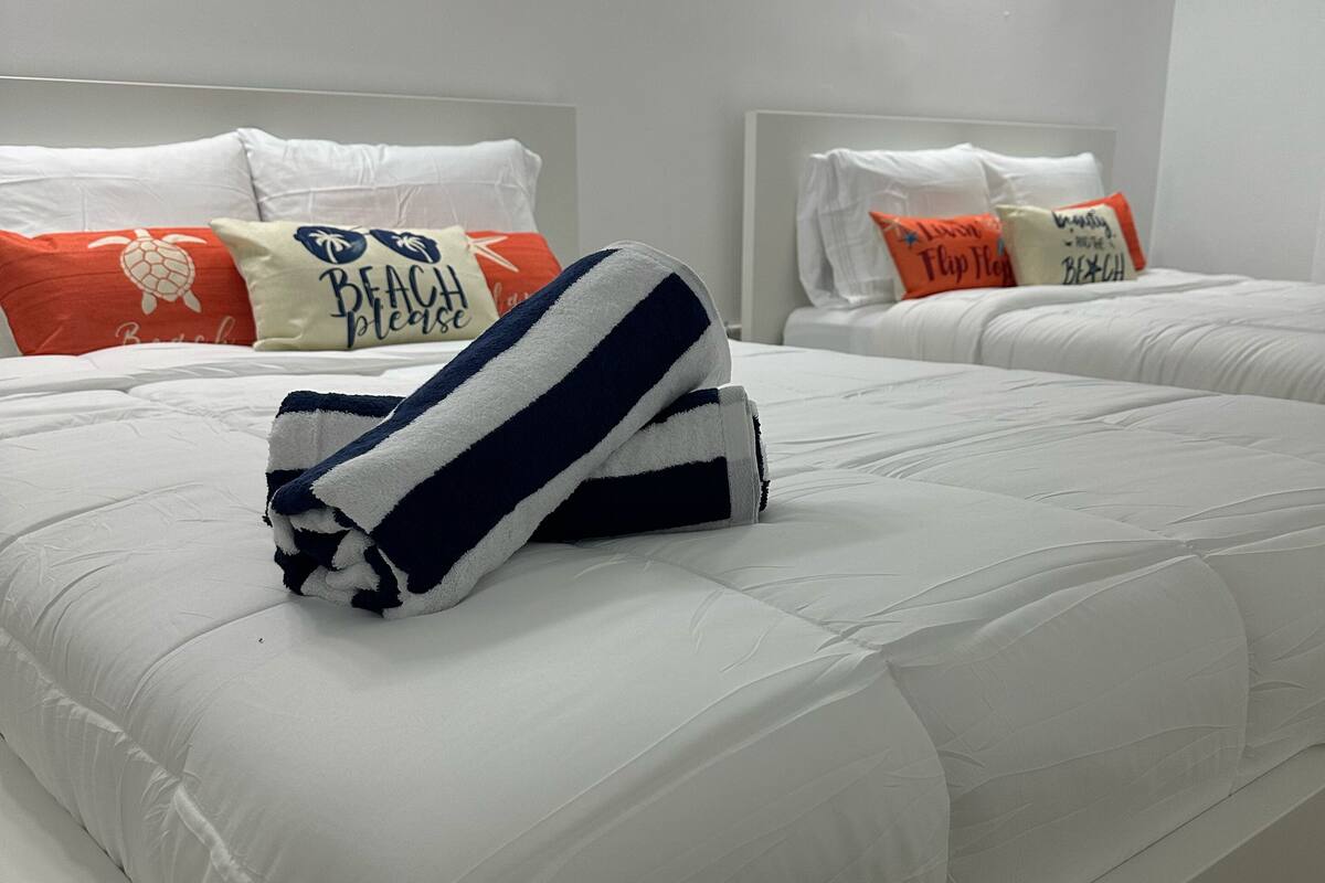 A hotel room with two beds, white bedding, and decorative pillows with text and images.