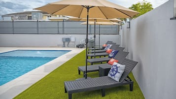 A poolside area with a lounge chair, a large umbrella, and a small pool.