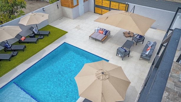 Uma área de piscina no terraço com várias espreguiçadeiras, guarda-sóis e um pequeno sofá.