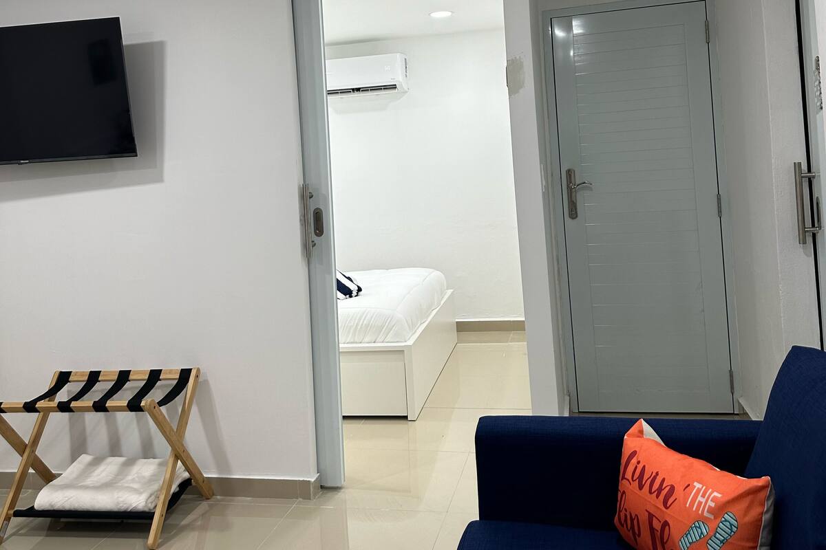 A modern room with a bed, a TV mounted on the wall, a blue sofa, and a door leading to another room.