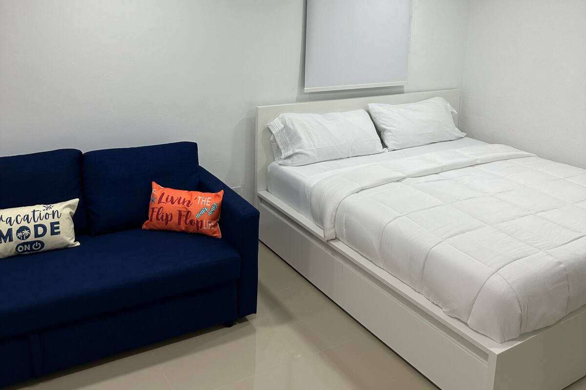 A modern bedroom with a white bed, a blue sofa, and two pillows.