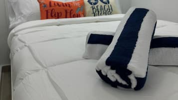 A neatly made bed with a white comforter and a blue and white striped towel. There are three pillows on the bed, each with different text and designs.