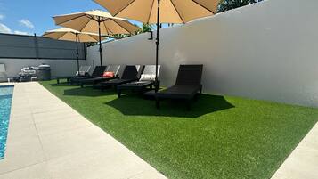 Un espace aménagé au bord de la piscine, avec une pelouse artificielle, des chaises longues et des parasols.