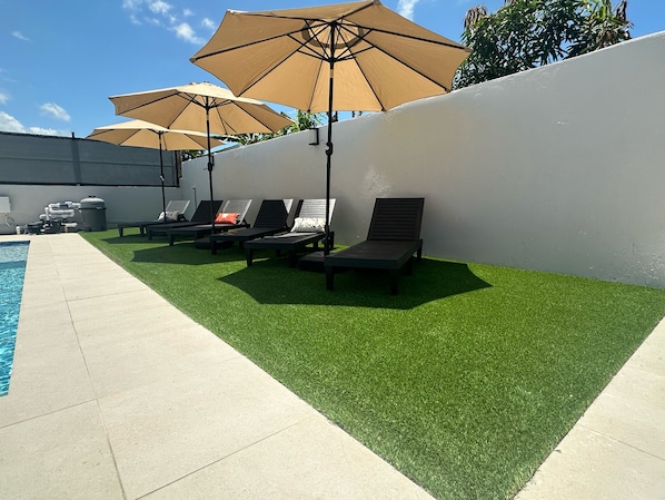 A poolside area with artificial grass, lounge chairs, and umbrellas. - Casa Toñita (Toa Baja)