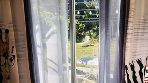 A room with sheer curtains, a view of an outdoor garden with a table and chairs, and a zebra-patterned pillow. - Gîte Rural Familial Entre Mer et Pays Cathare (Montséret)