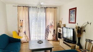 A living room with a blue sofa, a coffee table, a TV, and curtains with animal prints. - Gîte Rural Familial Entre Mer et Pays Cathare (Montséret)