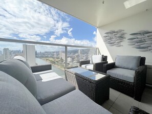 A balcony with wicker furniture, a glass table, and a city view.