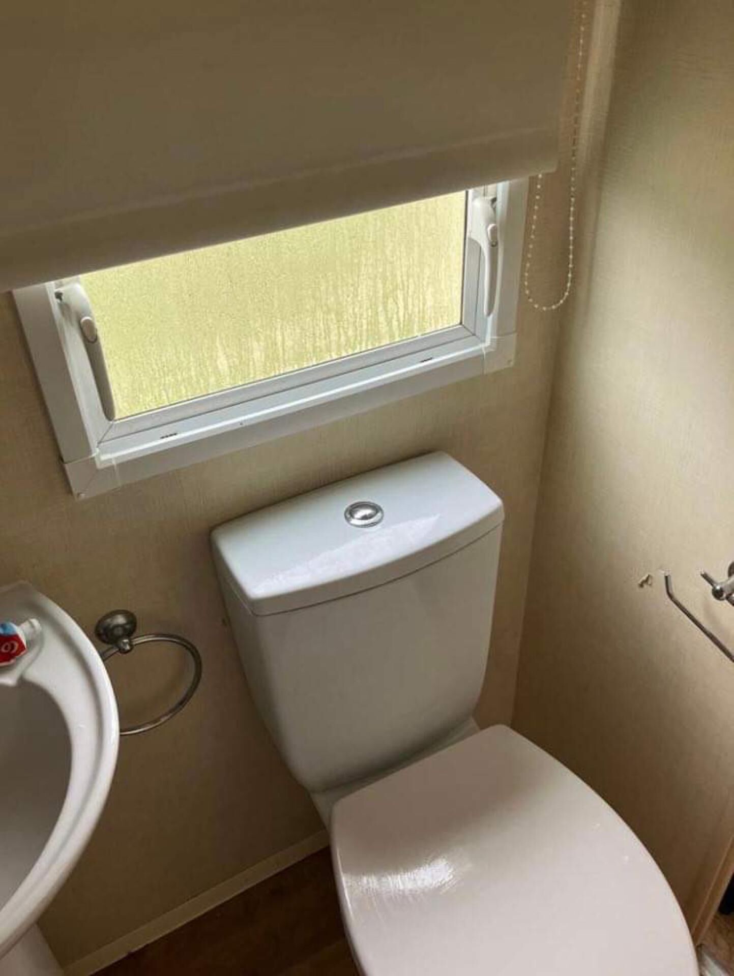 Un baño compacto con inodoro, un lavamanos pequeño y una ventana sobre el inodoro.