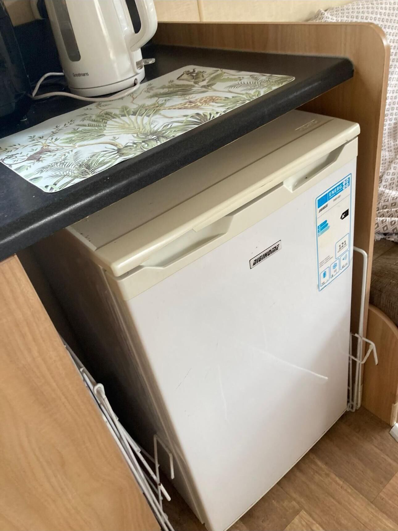 Un petit réfrigérateur doté d’un panneau de commande, placé sous un meuble en bois surmonté d’un plan de travail noir.