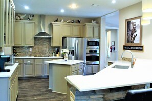 Une cuisine moderne avec des meubles en bois clair, des appareils en acier inoxydable, un îlot central et des œuvres d’art décoratives au mur.