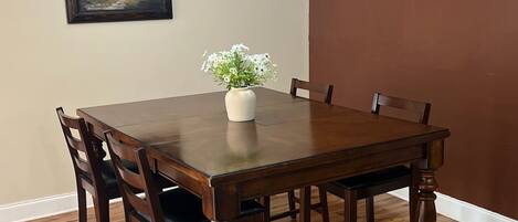Un comedor con mesa de madera, sillas, un jarrón con flores, un cuadro enmarcado, una lámpara en el techo y una decoración de estrellas en la pared.