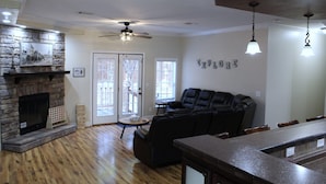 A spacious living room with a stone fireplace, a ceiling fan, and a black leather sofa. - The Den - Family Friendly Close to Fiesta Texas (San Antonio)