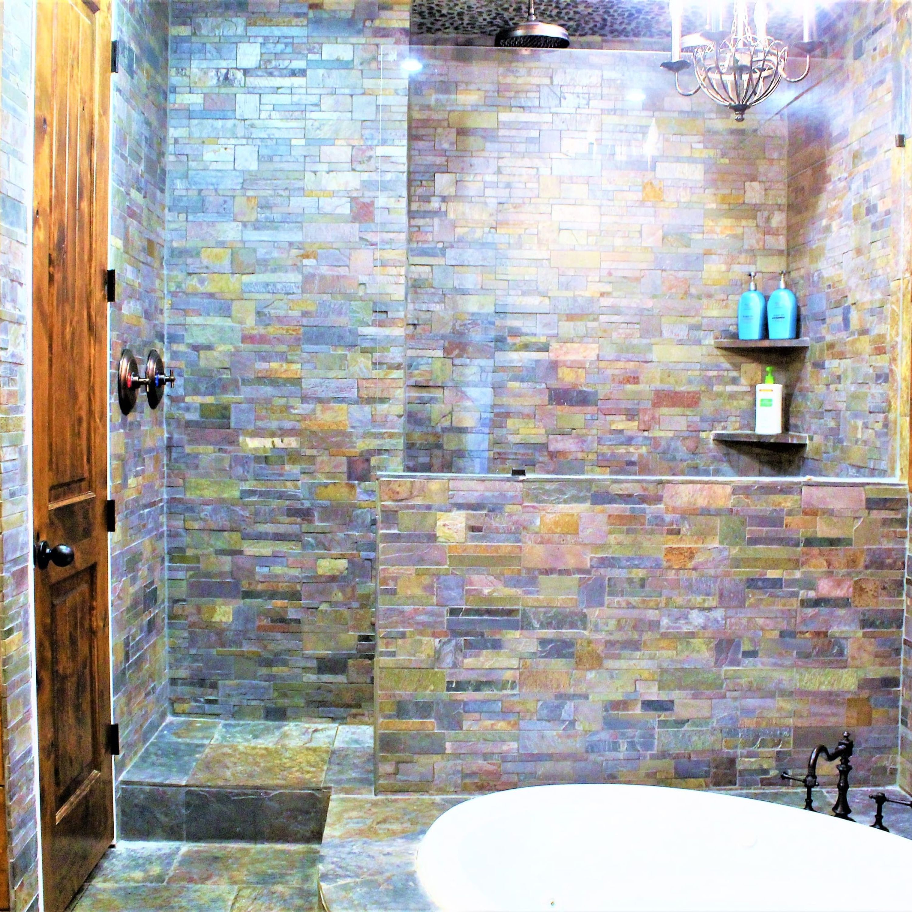 Un baño con pared de mosaico de piedra, puerta de madera y bañera blanca.