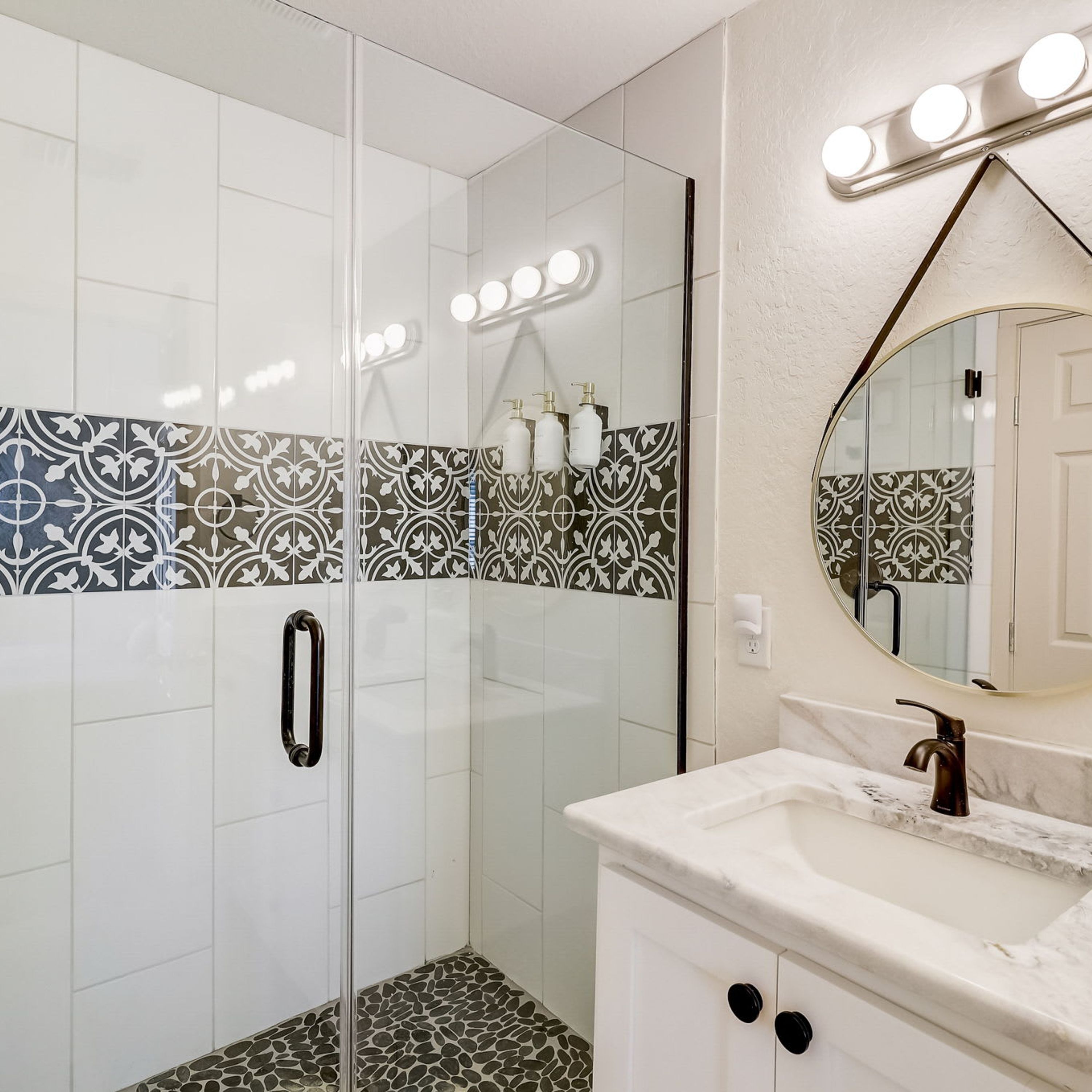 Un baño con cabina de ducha de vidrio, tocador con encimera de mármol y azulejos con diseño en las paredes.