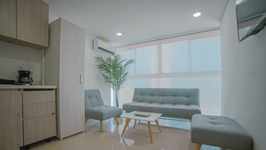 A modern living room with a grey sofa, two armchairs, a coffee table, and a kitchen area with cabinets and a coffee machine. - Armonioso loft de 1 Hab en Cartagena  (Cartagena)