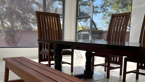 A dining area with a wooden table and chairs, large windows, and a bench. - The Baroness (Bulawayo)