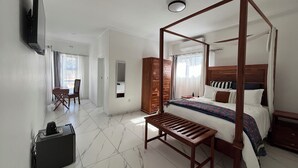 A spacious bedroom with a four-poster bed, a wooden bench, a desk with a chair, and a wardrobe. - The Baroness (Bulawayo)