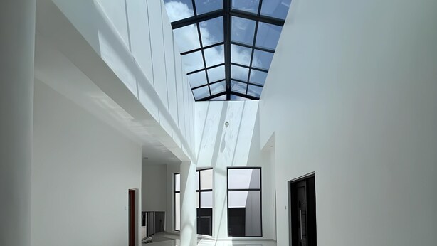 A spacious, modern interior with a high ceiling and skylight, featuring a long corridor with a tiled floor and large windows. - The Baroness (Bulawayo)