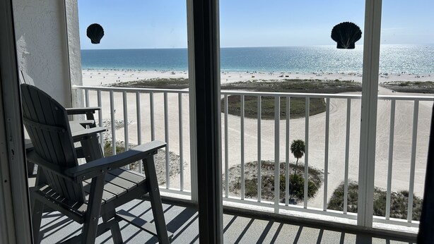 A balcony with a view of a beach, a chair, and a palm tree. - Paradise on the Beach (Treasure Island)