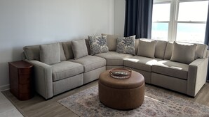 A modern living room with a beige sectional sofa, a wooden side table, and a patterned rug. - Paradise on the Beach (Treasure Island)