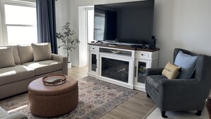 A living room with a sofa, ottoman, and armchair, a flat-screen TV, and a fireplace. - Paradise on the Beach (Treasure Island)