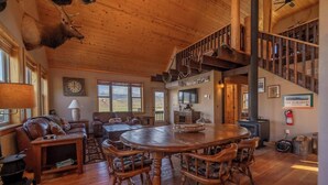 Ein großzügiges Wohnzimmer mit einem großen Esstisch aus Holz, Ledersofas und einem Kamin.