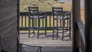 Eine Holzterrasse mit Stühlen und einem Tisch, mit Blick auf eine Berglandschaft mit einem See.