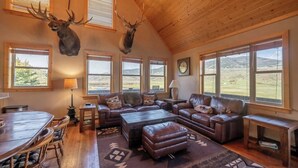 Ein geräumiges Wohnzimmer mit hoher Decke, Ledersofas, einem Couchtisch und einem Essbereich mit Holztisch und Stühlen.
