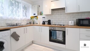 A modern kitchen with white cabinets, a built-in oven, a microwave, and a coffee maker. - 3-bed House in London Near the O2 Arena & Excel (London)