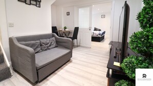 A modern living room with a grey sofa, a flat-screen TV, and a small table with a plant. - 3-bed House in London Near the O2 Arena & Excel (London)