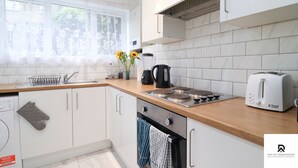 A modern kitchen with white cabinets, a wooden countertop, a sink, a stove, and a toaster. - 3-bed House in London Near the O2 Arena & Excel (London)
