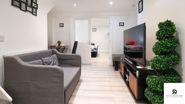 A modern living room with a grey sofa, a flat-screen TV, and a small table. - 3-bed House in London Near the O2 Arena & Excel (London)