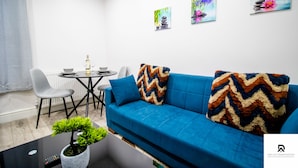 A modern living room with a blue sofa, a small dining table, and a potted plant. - 2-bed Near the O2 Arena & Excel & Free Parking (London)