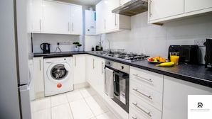 A modern kitchen with white cabinets, a built-in washing machine, a stove, and a microwave. - 2-bed Near the O2 Arena & Excel & Free Parking (London)