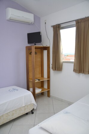 Una habitación con dos camas, un televisor sobre un mueble de madera, aire acondicionado y una ventana con cortinas.