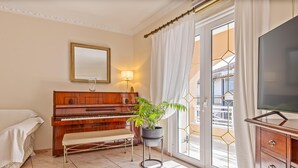 A hotel room with a piano, a bench, a potted plant, a TV, and a balcony with a view.