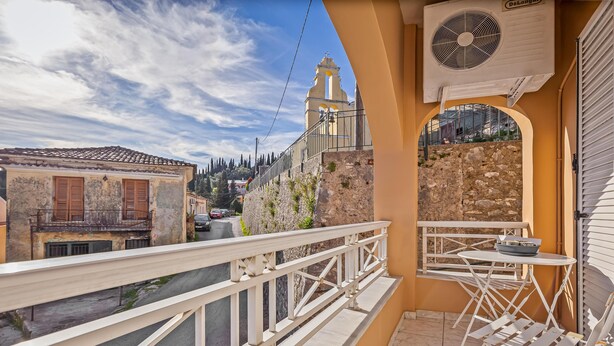 A balcony with a white railing, a table with chairs, and a view of a church and buildings in the background.