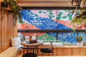 A modern outdoor seating area with a wooden bench and a round table, a colorful mural on the wall, and potted plants. - OBO Casa Modern Lux Design Loft Ipanema Beach (Rio de Janeiro)