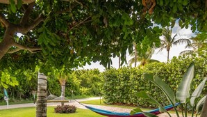 A hammock under a tree in a well-maintained garden with grass and various plants. - Clean Spacious Waterfront 2bd 2ba Sleeps 8 (Fort Pierce)