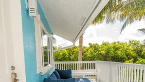 A covered outdoor seating area with wicker furniture and blue cushions, white railings, and a view of lush greenery. - Clean Spacious Waterfront 2bd 2ba Sleeps 8 (Fort Pierce)