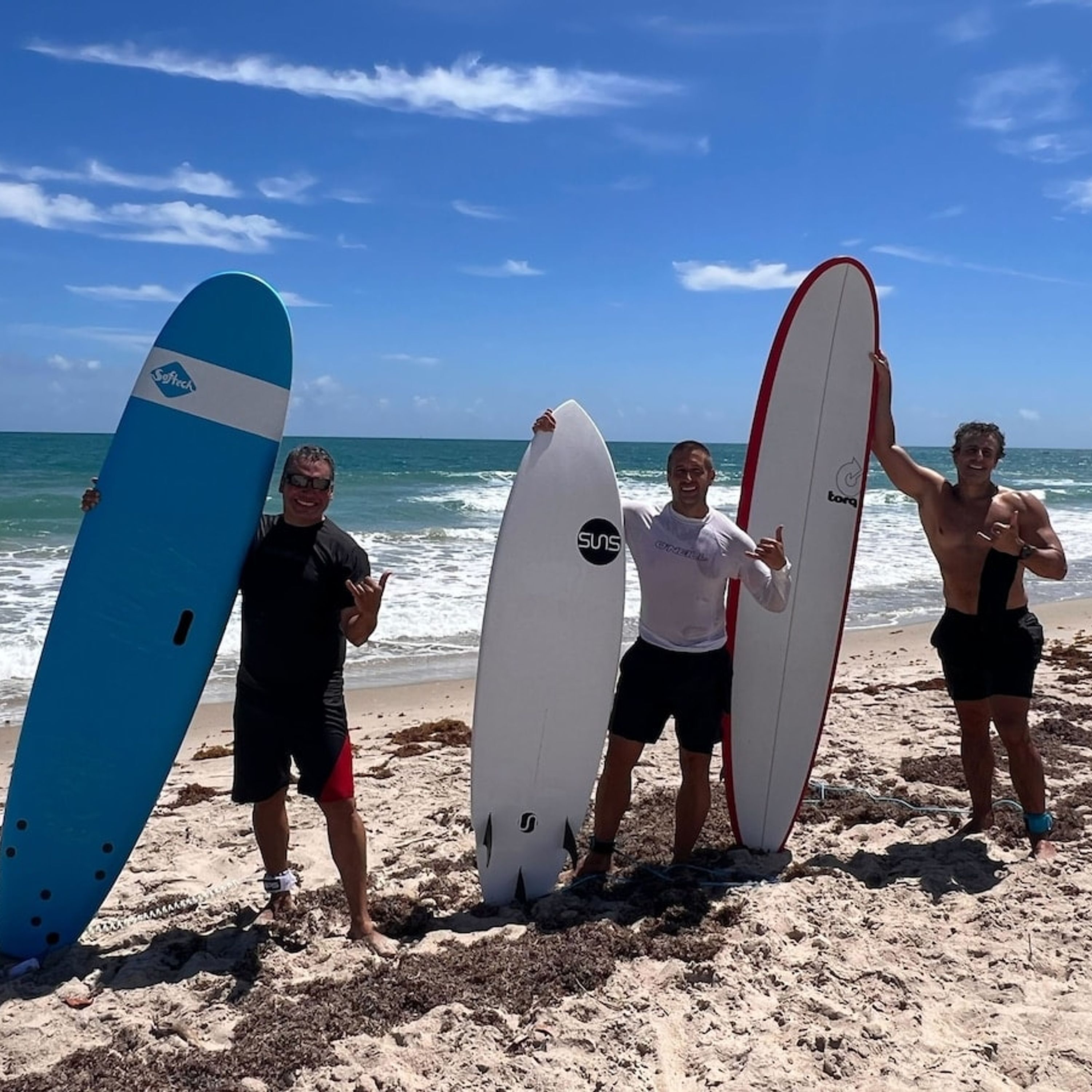 Three people holding surfboards on a beach with the ocean in the background.
