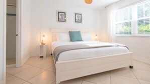 Un dormitorio con cama, ventilador de techo, lámparas de noche y cuadros en la pared.
