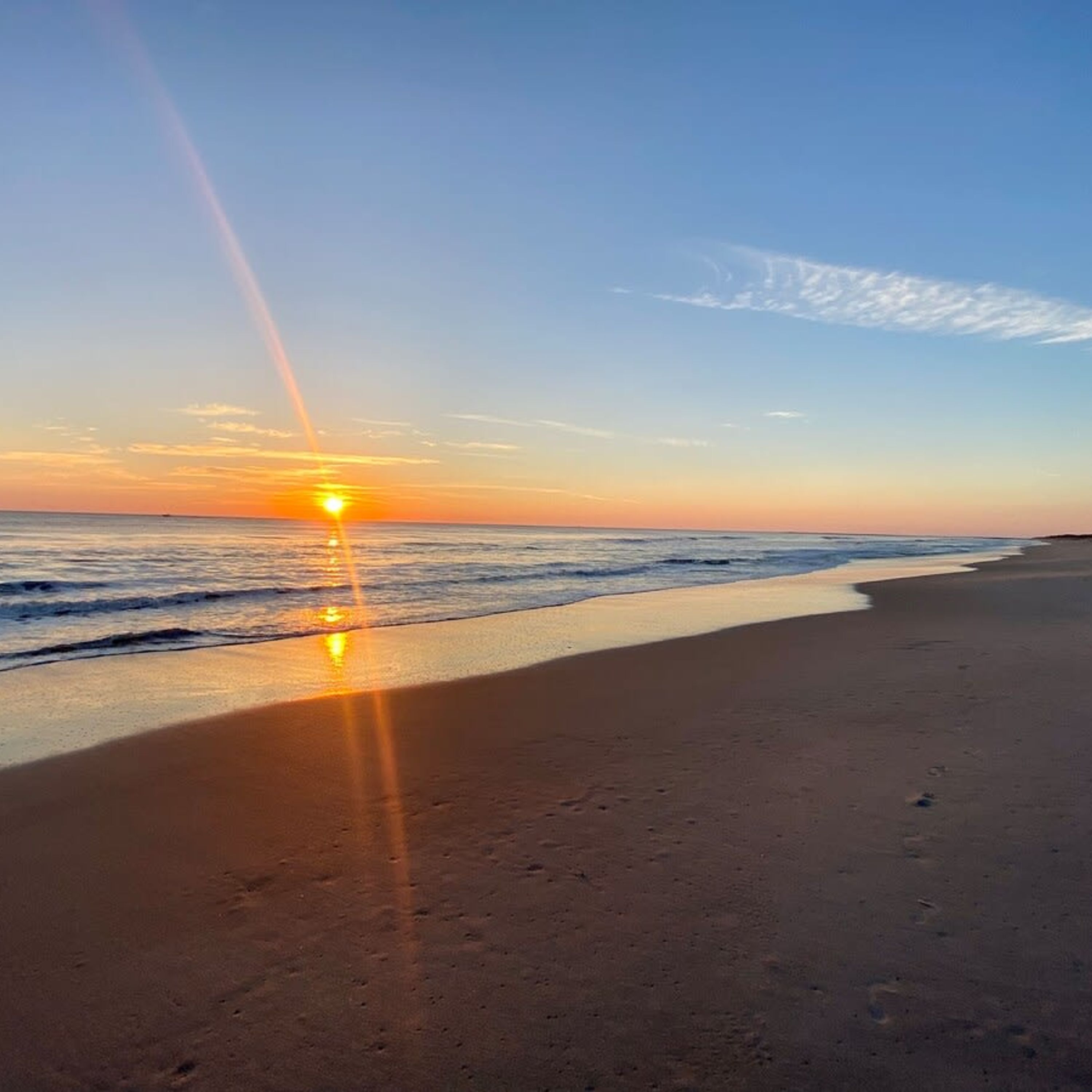 Une plage où l’on peut admirer le coucher de soleil sur l’océan, avec un ciel dégagé et des empreintes de pas bien visibles dans le sable.