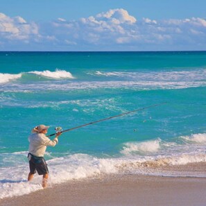 A person fishing on a beach with clear blue water and waves.