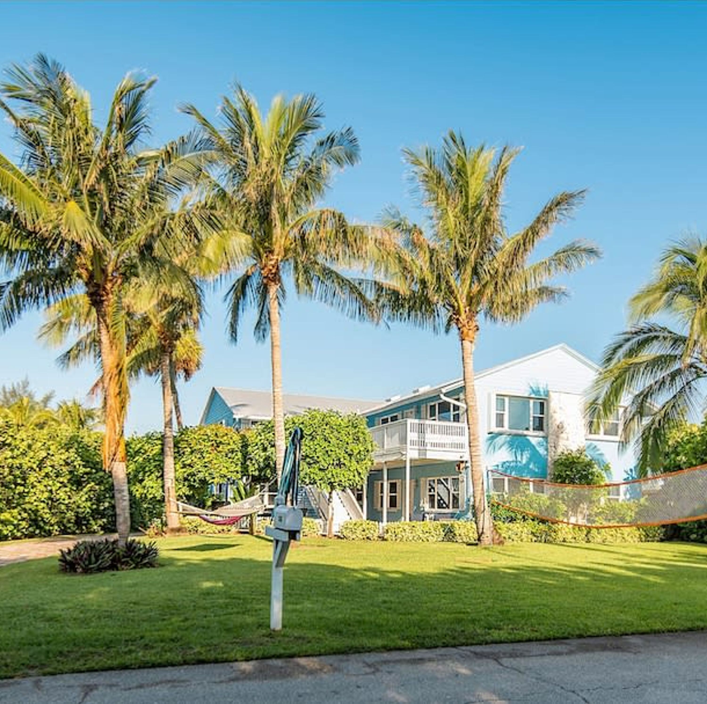 A beachfront property with palm trees, a grassy lawn, and a house with a balcony.
