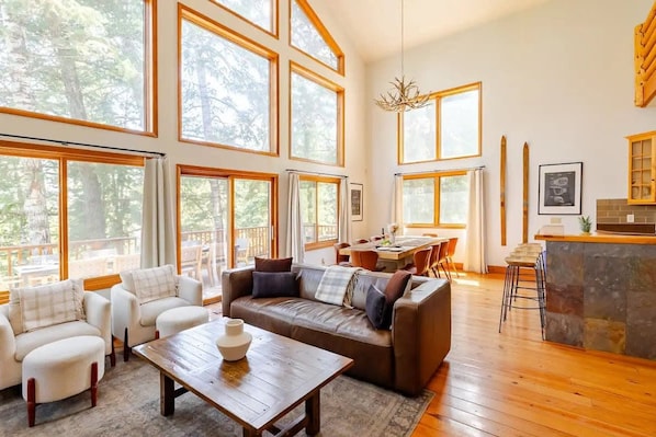 Amplia sala de estar con ventanas grandes, una mesa de comedor de madera, un sofá y una zona de cocina con una isla de piedra.