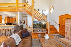 A modern interior with a wooden staircase, a living area with a sofa and coffee table, a kitchen with wooden cabinets, and a large TV on the wall. - Park City Mountain Retreat 4BR Hot Tub Fire Pit (Park City)