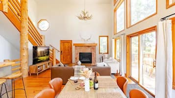A spacious living area with a fireplace, wooden staircase, and large windows.