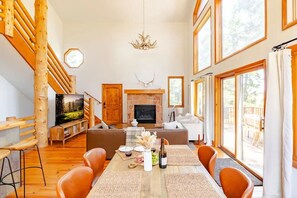 A spacious living area with a fireplace, wooden staircase, and large windows. - Park City Mountain Retreat 4BR Hot Tub Fire Pit (Park City)