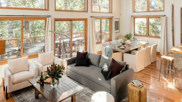 Un salón amplio con ventanas grandes, un ventilador de techo y una zona de comedor con mesa y sillas.